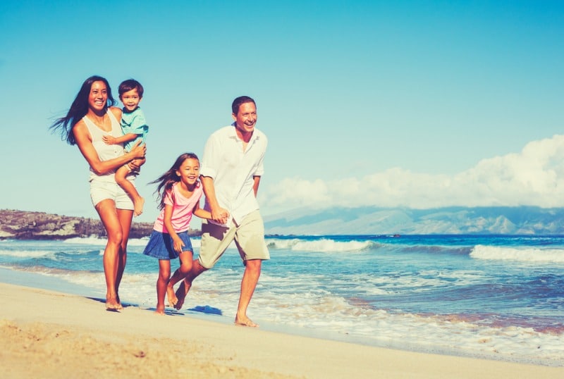 Hawaii Vacation Rentals: A young family of four smile as they walk along the shoreline of Maui near their vacation rental.