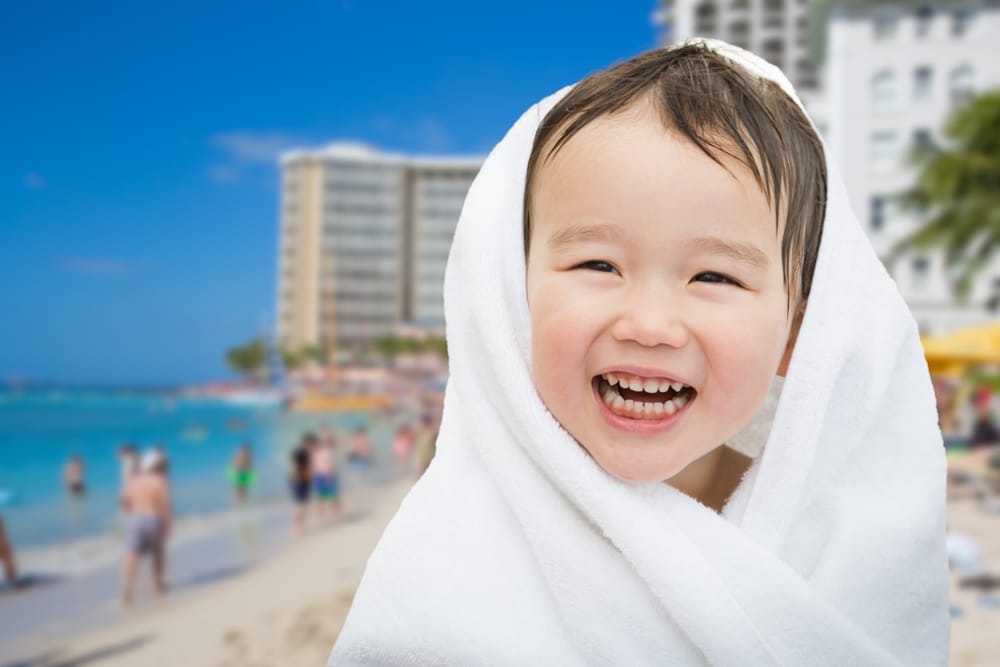 Things to Do in Oahu With Kids: A young boy smiles while drying off after a swim with the beach in the background.